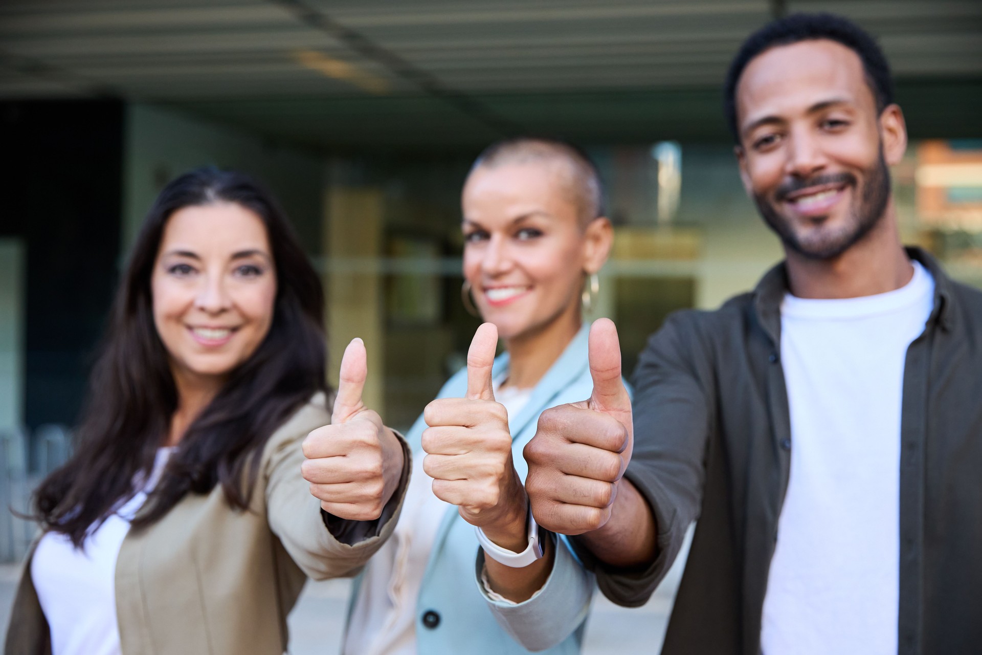Happy diverse coworkers in stylish outfits smiling and showing thumbs up while looking at camera during break
