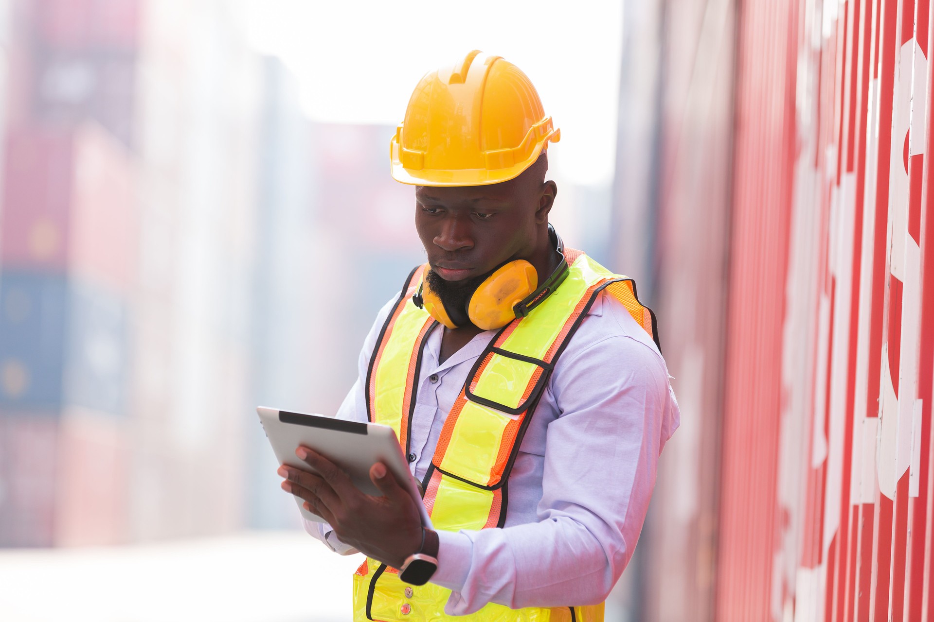 African American male container yard worker working and checking container boxes before loading at commercial dock site. Black male people worker inspecting container boxes from cargo freight ship